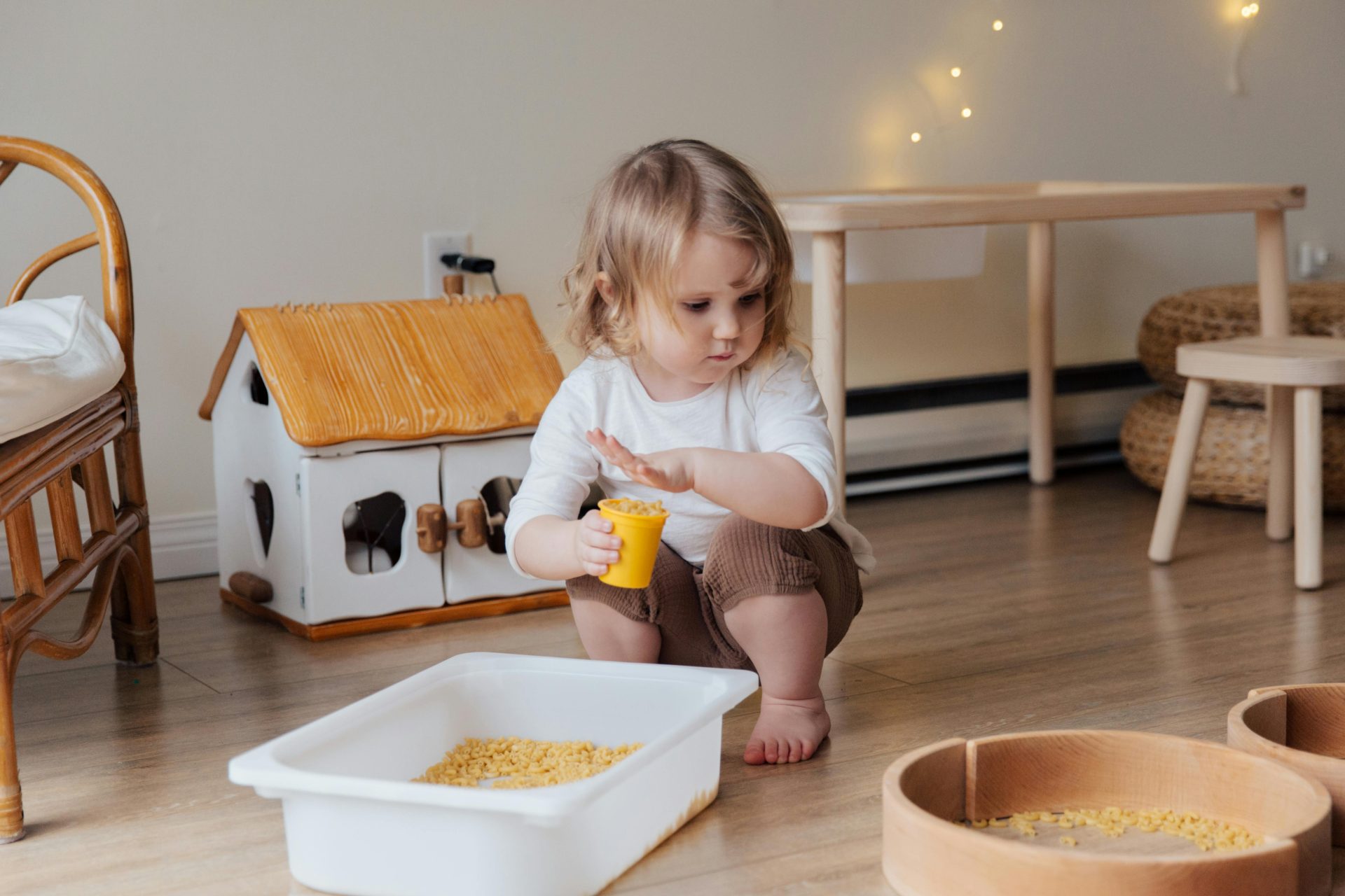 A young child playing with macaroni in a cozy indoor playroom setting.