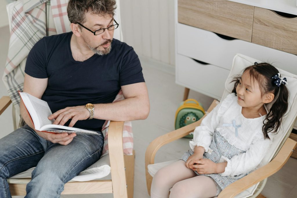 A father reading a book to his smiling daughter indoors, bonding activity.
