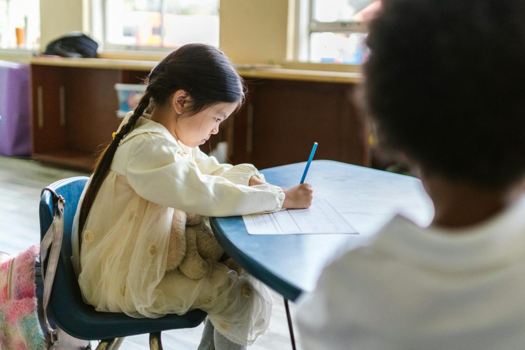 A young child intensely focused on writing at a classroom table, showing concentration and learning.