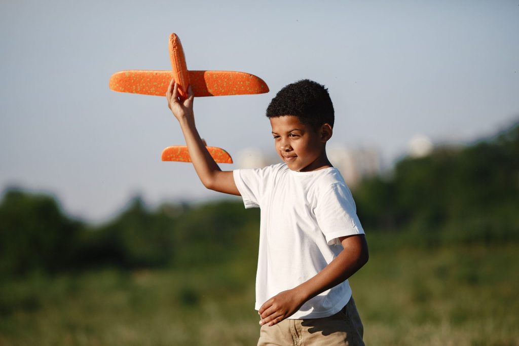 Young boy joyfully playing with a toy airplane outdoors on a sunny day.